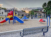 Thumbnail 27 of 27 - A playground with a red slide, blue slide, and a black bench.