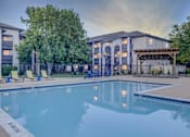 Thumbnail 2 of 27 - A swimming pool in front of a building with a patio area.