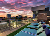 Thumbnail 29 of 31 - A modern building with a pool and lounge chairs is illuminated by the setting sun.