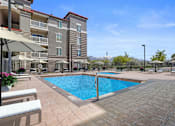 Thumbnail 18 of 29 - A large swimming pool surrounded by a tiled patio and apartment buildings.