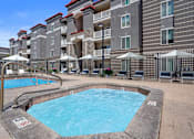 Thumbnail 20 of 29 - A swimming pool surrounded by lounge chairs and umbrellas in front of a multi-story apartment building.