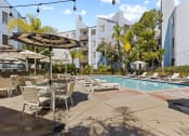 Thumbnail 12 of 53 - a swimming pool with tables and umbrellas and buildings in the background at Enclave, Paramount, CA 90723