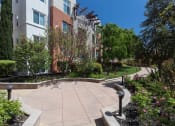 Thumbnail 15 of 30 - walkway outside apartment building surrounded by greenery