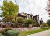 Thumbnail 27 of 33 - large homes on top of a stone retaining wall with trees and bushes