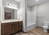 Thumbnail 25 of 50 - A white toilet sits in a bathroom with wood floors and white walls.
