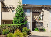 Thumbnail 14 of 18 - A beige two-story apartment building with a tree in front.