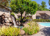 Thumbnail 15 of 18 - A pool with a waterfall and a tree in the middle of a garden.