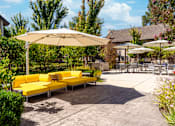 Thumbnail 3 of 18 - A yellow couch is sitting under a white umbrella in a courtyard.