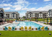 Thumbnail 1 of 28 - an outdoor pool with yellow and blue chairs around it and apartments in the background