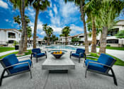 Thumbnail 45 of 52 - A patio with blue chairs and a fire pit surrounded by palm trees.