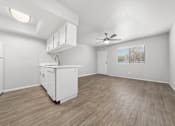 Thumbnail 7 of 21 - an empty living room with a kitchen and a ceiling fan