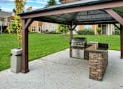 Thumbnail 24 of 30 - A covered patio with a grill and a trash can.