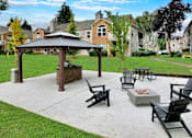 Thumbnail 25 of 30 - A gazebo is surrounded by black chairs and a fire pit in a grassy area.