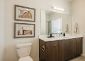 Thumbnail 12 of 20 - A white toilet sits next to a bathroom vanity with a mirror above it.