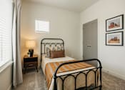 Thumbnail 9 of 20 - A bedroom with a bed, nightstand, and two pictures on the wall.