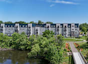 Thumbnail 29 of 35 - A row of modern apartment buildings are surrounded by trees and a small lake.
