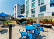 Thumbnail 52 of 54 - an outdoor patio with blue tables and chairs and an apartment building in the background