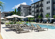 Thumbnail 56 of 59 - A pool area with sun loungers and umbrellas in front of apartment buildings.