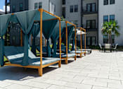 Thumbnail 58 of 59 - A row of wooden daybeds with green canopies are lined up on a patio.