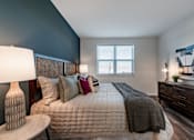 Thumbnail 19 of 36 - A bedroom with a bed, nightstand, and a painting on the wall.