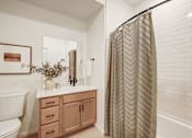 Thumbnail 9 of 23 - A bathroom with a white toilet, a sink with a mirror, a plant, and a shower curtain.