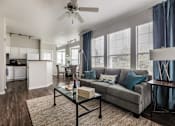 Thumbnail 1 of 14 - A living room with a grey couch and a glass coffee table.