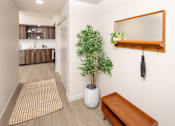 Thumbnail 16 of 34 - A hallway with a potted plant, a mirror, and a bench.