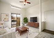 Thumbnail 10 of 13 - A living room with a white couch, a wooden coffee table, a flat screen TV, and a ceiling fan.