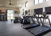 Thumbnail 22 of 34 - A gym with treadmills, elliptical machines, and a fan.