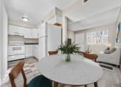 Thumbnail 3 of 23 - Dining area next to a white kitchen with wood flooring and natural light.