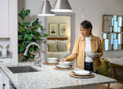 Thumbnail 17 of 29 - a woman placing dishes on a counter in a kitchen