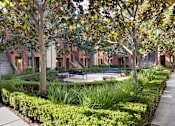 Thumbnail 14 of 24 - A courtyard with a bench and a tree in front of apartment buildings.