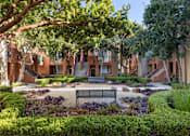 Thumbnail 15 of 24 - A bench is situated in the middle of a garden with a building in the background.
