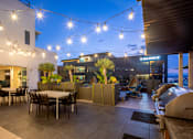 Thumbnail 4 of 29 - Rooftop patio with string lights and tables and chairs at AV8 apartments for rent in San Diego, CA.