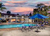 Thumbnail 11 of 22 - A poolside area with lounge chairs and umbrellas is set against a sunset sky.