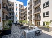 Thumbnail 37 of 48 - an outdoor patio with a firepit and tables surrounded by apartment buildings at VORA LUX, San Diego California