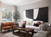 Thumbnail 4 of 37 - A living room with a white couch, a brown chair, a coffee table, and a large abstract painting on the wall.