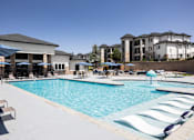 Thumbnail 24 of 37 - A large swimming pool with lounge chairs and umbrellas in front of a building.