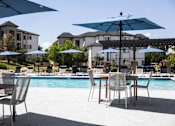 Thumbnail 25 of 37 - A poolside table with chairs and umbrellas is set up by the pool.
