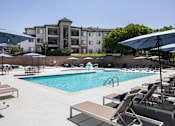 Thumbnail 23 of 37 - A pool with sun loungers and umbrellas in front of a building.