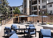 Thumbnail 27 of 37 - A patio with blue chairs and a fire pit in front of a building.