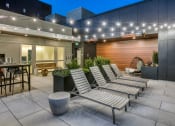 Thumbnail 14 of 30 - a group of lounge chairs in front of a building with lights on it