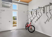 Thumbnail 15 of 22 - A red bicycle is parked in a garage with a white wall and a bike rack.
