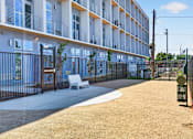 Thumbnail 17 of 22 - A modern apartment complex with a fenced courtyard and a bench.