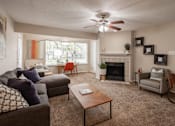 Thumbnail 10 of 39 - A living room with a grey couch, a brown coffee table, a fireplace, and a ceiling fan.