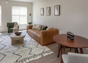 Thumbnail 14 of 34 - A living room with a green chair, a brown couch, and a white rug.