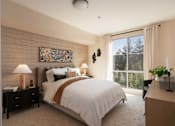 Thumbnail 5 of 28 - A bedroom with a large bed, a lamp, a painting, and a window with a view of trees.