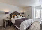 Thumbnail 18 of 22 - A bedroom with a large bed and a nightstand with a lamp.
