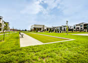 Thumbnail 20 of 26 - A park with a walking path and benches in front of a building.