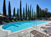 Thumbnail 11 of 26 - A pool surrounded by tall trees and lounge chairs at The Casas Apartments, San Diego, CA, 92126